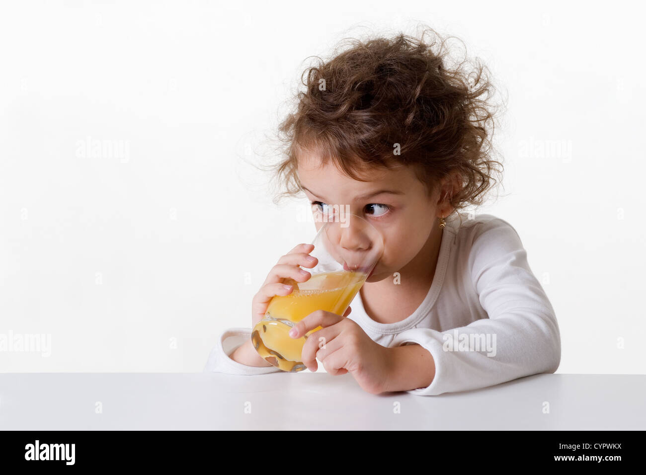 Kaukasische Mädchen, ca. 5-6 Jahre alt, braune Augen, lockiges Haar, trinkt ein Glas Orangensaft, isoliert auf weißem Hintergrund Stockfoto