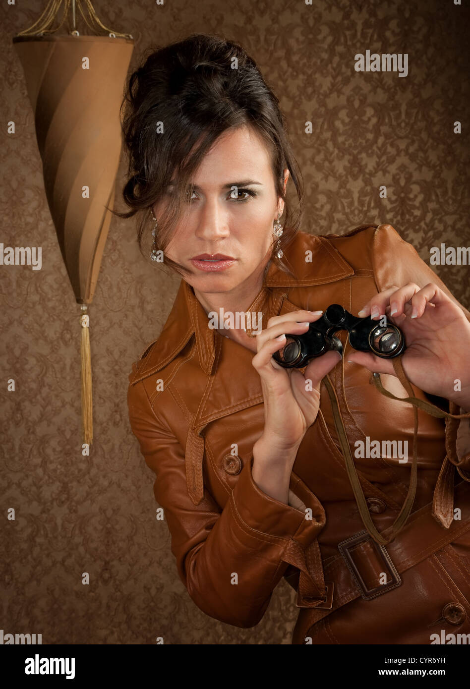 Schöne Spion mit dem Fernglas im Ledermantel Stockfoto