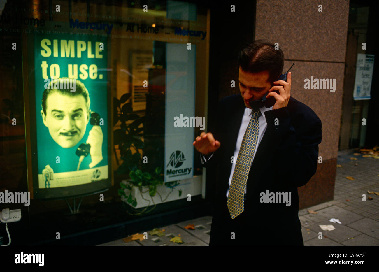 Vor einer Anzeige für Merkur, der 90er Jahre mobile Telefon Netzwerk-Provider, eine Stadt Arbeitskraft nutzt sein Handy in einer Londoner Straße. Stockfoto