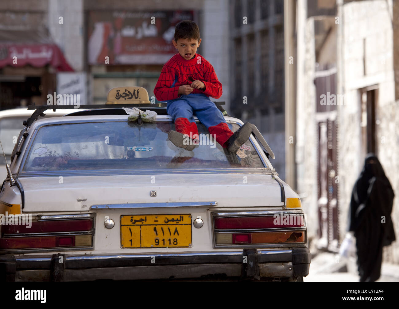 Kind Spiderman Anzug sitzt auf der Oberseite einen Mietwagen In eine Straße von Sanaa, Jemen Stockfoto