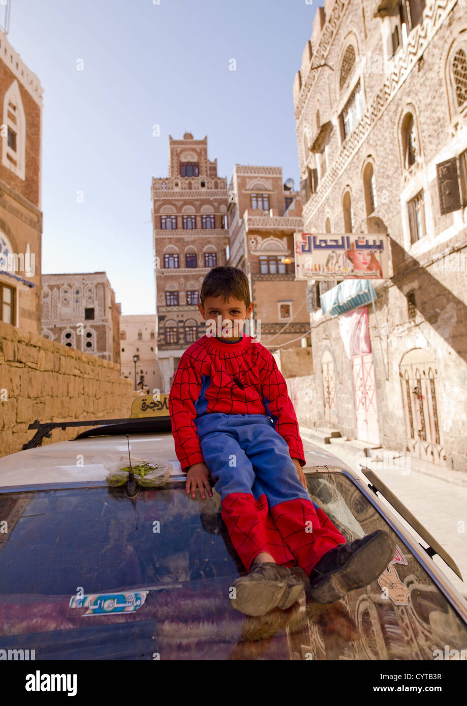 Lächelndes Kind trägt einen Spiderman-Anzug und Erwachsenen Schuhe, sitzt auf der Spitze eines Autos, Sanaa, Jemen Stockfoto