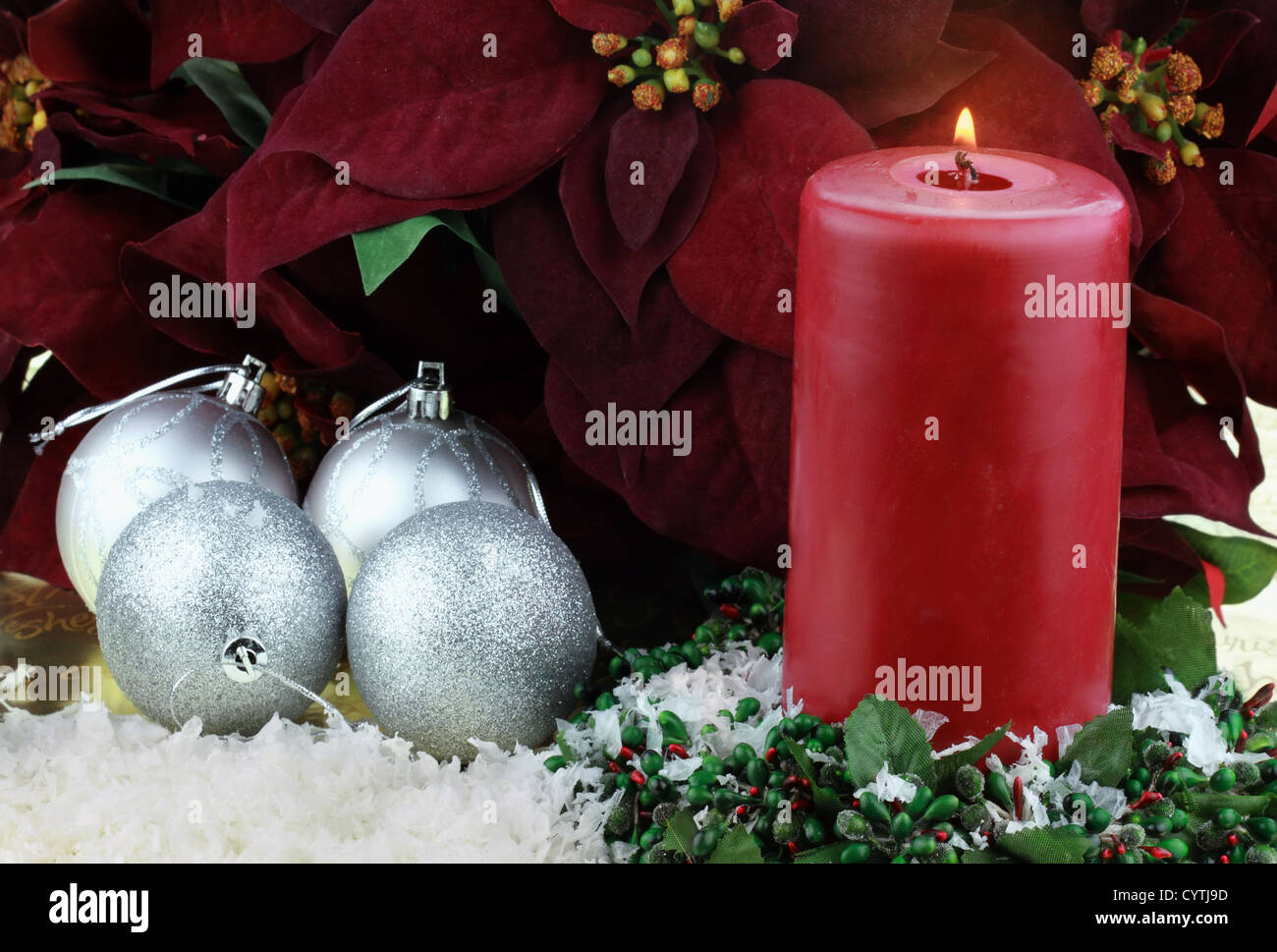 Brennende Weihnachtskerze umgeben von Reich Burgund farbigen Weihnachtssterne, Silberschmuck und Schnee. Stockfoto