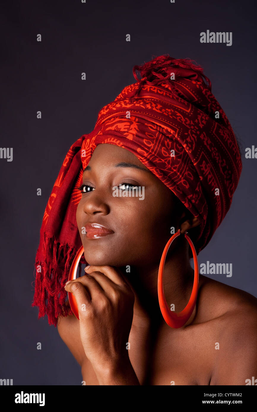 Schöne afro-amerikanische Frau trägt ein traditionelles tribal rot orange Kopftuch und große orange Creolen, ihr Kinn mit der Hand, isoliert zu unterstützen. Stockfoto