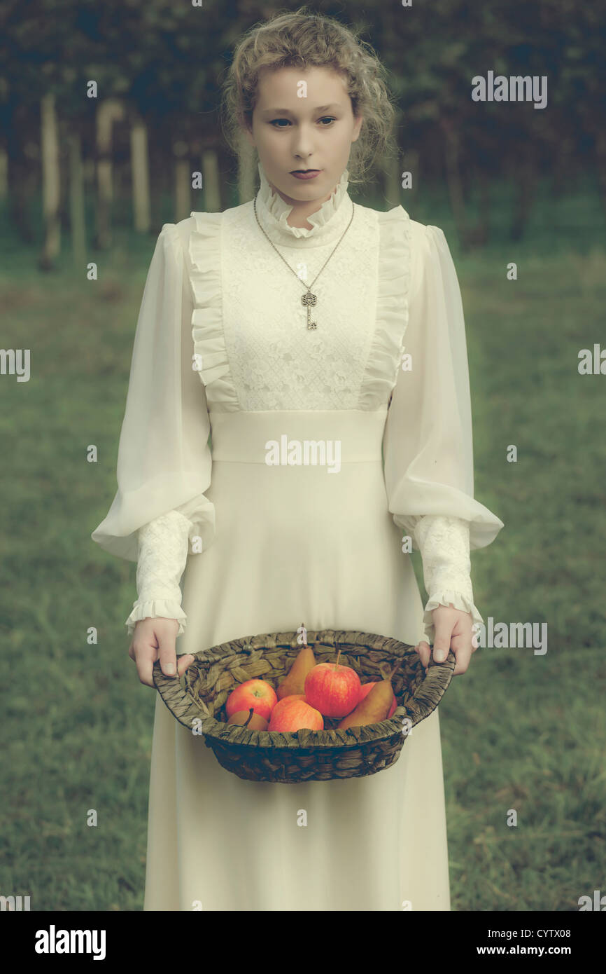 eine Frau in einem weißen Kleid edwardian hält einen Korb mit Früchten Stockfoto