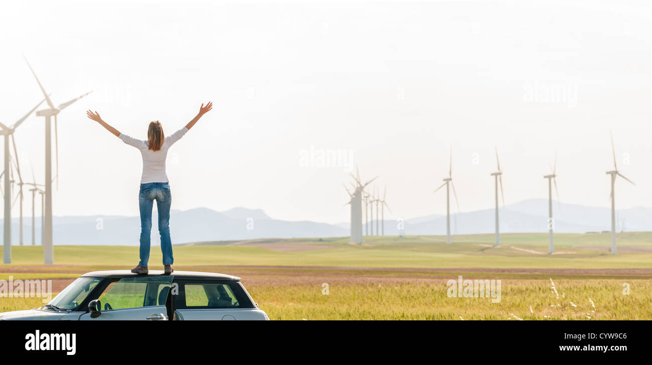 Junge Frau stand am Anfang von ihrem Auto mit erhobenen Händen. Mädchen in gelben Herbst Feld mit Windrädern im Hintergrund. Stockfoto