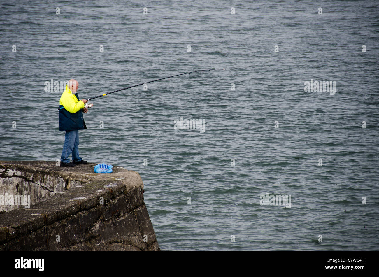 BEAUMARIS, Wales – Ein Fischer wirft seine Linie von einer Steinmauer entlang der Küste von Beaumaris auf der Isle of Anglesey. Die Szene überblickt die Menai-Straße, mit den Bergen von Snowdonia in der Ferne. Beaumaris liegt an der Ostküste von Anglesey und ist bekannt für seine historische Burg und seine Fischermöglichkeiten an der Küste. Die Stadt liegt an der Menai-Straße, die Anglesey vom Festland von Wales trennt. Die Gegend zieht sowohl Freizeitangler als auch Besucher an, die von der walisischen Küstenlandschaft angezogen werden. Von hier aus hat man einen Blick über die Meerenge in Richtung der Snowdonia-Gebirgskette Stockfoto BEAUMARIS, Wales – Ein Fischer wirft seine Linie von einer Steinmauer entlang der Küste von Beaumaris auf der Isle of Anglesey. Die Szene überblickt die Menai-Straße, mit den Bergen von Snowdonia in der Ferne. Beaumaris liegt an der Ostküste von Anglesey und ist bekannt für seine historische Burg und seine Fischermöglichkeiten an der Küste. Die Stadt liegt an der Menai-Straße, die Anglesey vom Festland von Wales trennt. Die Gegend zieht sowohl Freizeitangler als auch Besucher an, die von der walisischen Küstenlandschaft angezogen werden. Von hier aus hat man einen Blick über die Meerenge in Richtung der Snowdonia-Gebirgskette Stockfoto