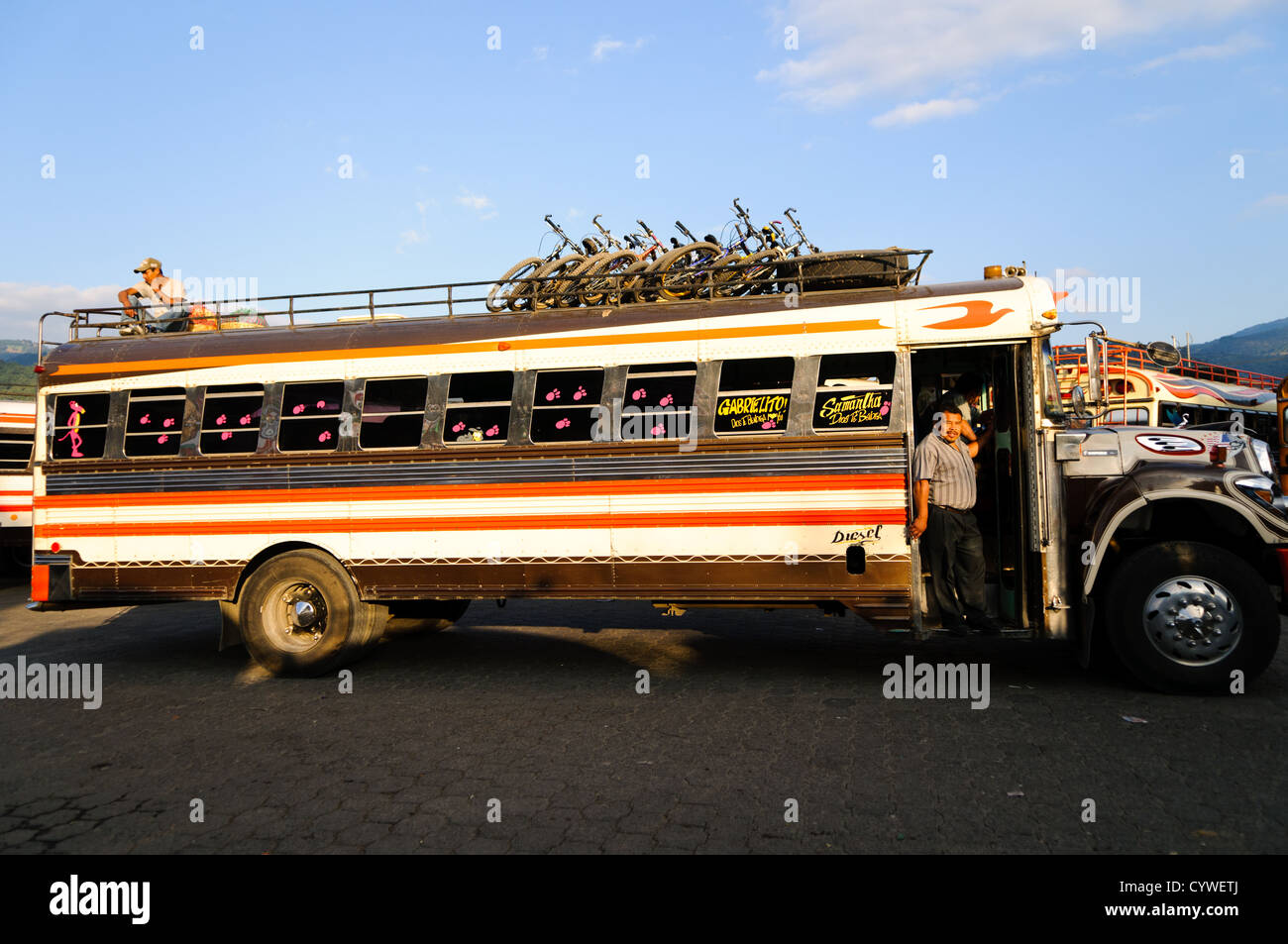 ANTIGUA GUATEMALA, Guatemala – bunt bemalte Hühnerbusse säumen eine Straße in Antigua Guatemala. Diese umgestalteten amerikanischen Schulbusse mit lebendigen Designs und Chromaccessoires sind bereit, Einheimische und abenteuerlustige Touristen zu transportieren und verkörpern Guatemalas lebendige Verkehrskultur vor dem Hintergrund der kolonialen Architektur. Stockfoto