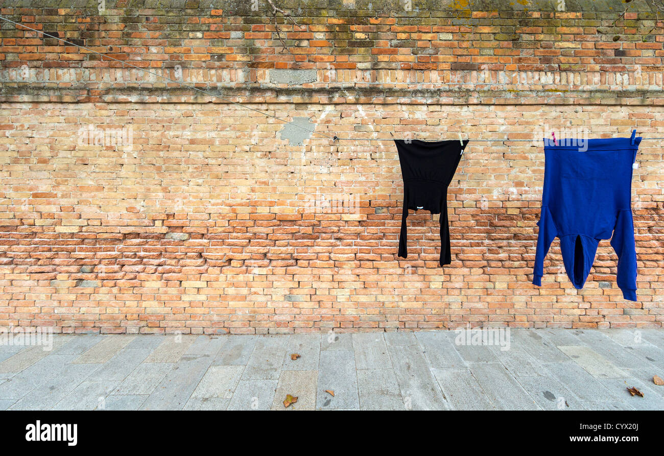Waschen hängen zum Trocknen vor einer Mauer, bestehend aus einem dünnen schwarzen Top und einer blauen Sweatshirt mit Kapuze Stockfoto