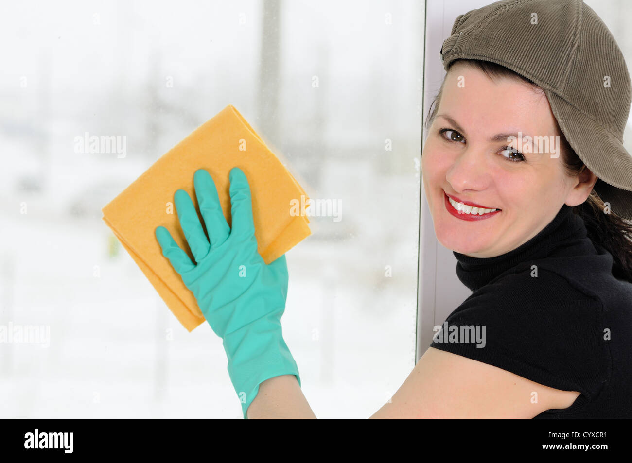 Die Frau mit einem gelben Lappen wäscht ein Fenster Stockfoto