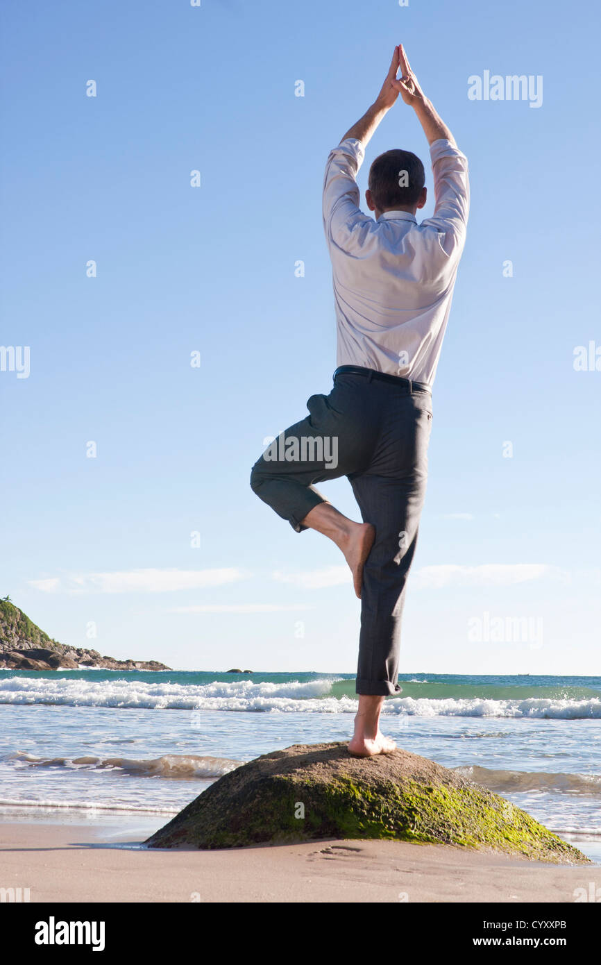 Geschäftsmann Gleichgewichtherstellung Übung auf einem Felsen am Strand Stockfoto