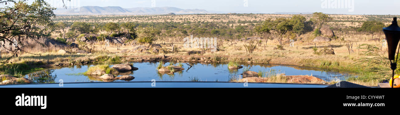 Blick vom hinteren Pool-Deck der Bilia Lodge mit Infinity-Pool und Wasserstelle unten. Serengeti Nationalpark, Tansania Stockfoto