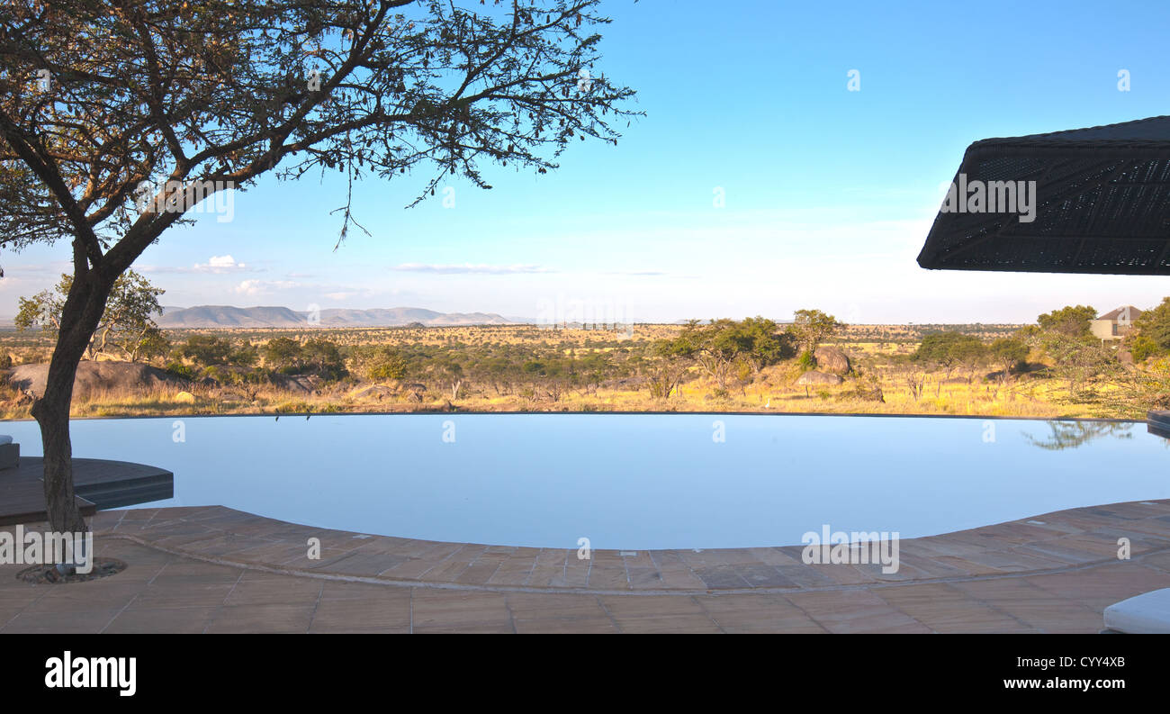 Blick vom hinteren Pool-Deck der Bilia Lodge mit Infinity-Pool und Wasserstelle unten. Serengeti Nationalpark, Tansania Stockfoto
