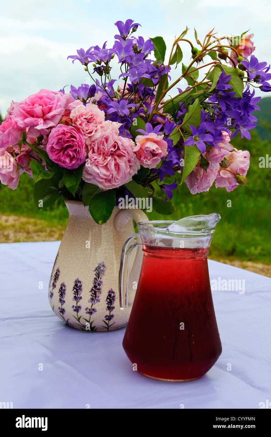 Ein Blumenstrauß und ein Becher mit roten Saft im Garten Stockfoto