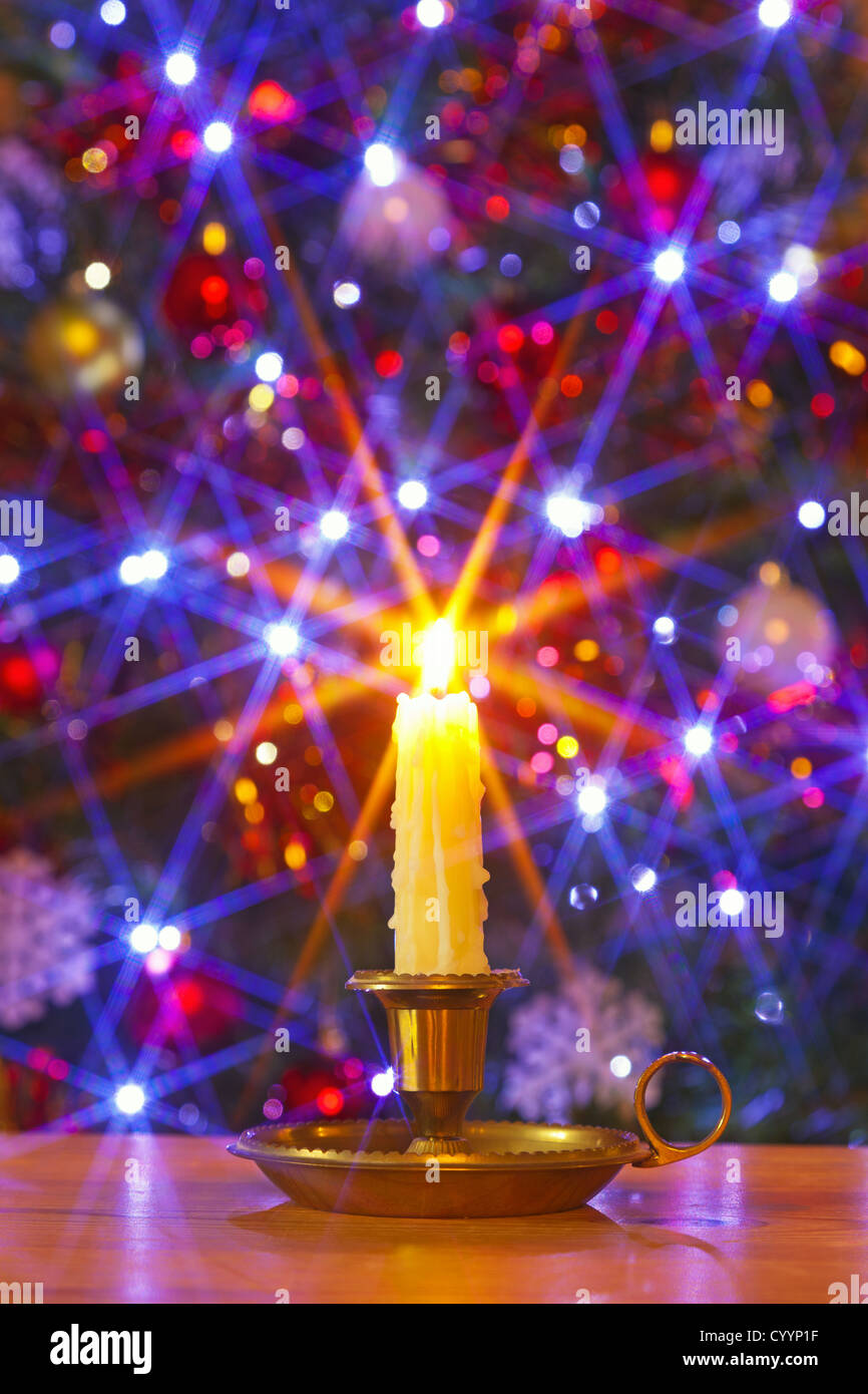 Einen tropfenden Wachskerze in Messing Halterung gegen einen Weihnachtsbaum mit Dekorationen und Lichterketten Stockfoto