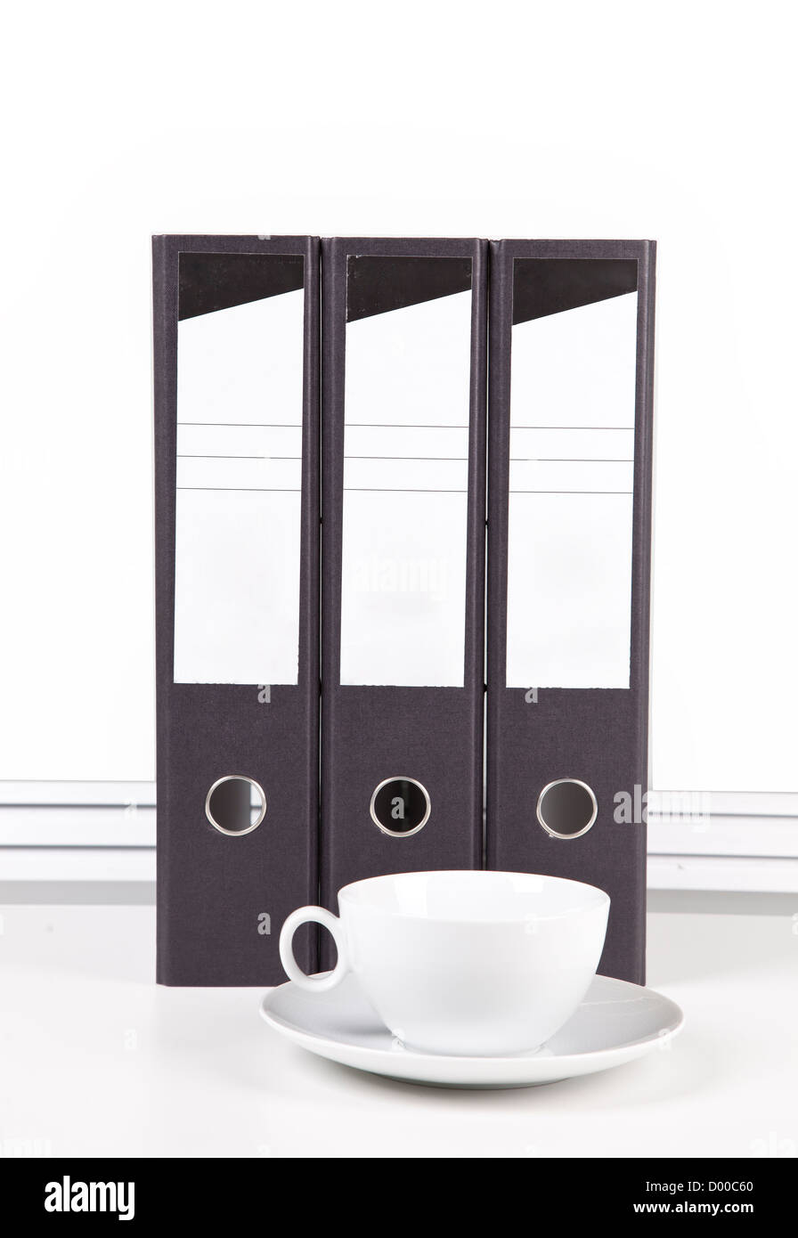 Milchkaffee-Tasse und Untertasse vor Ordner am Schalter gegen weiße Wand Stockfoto