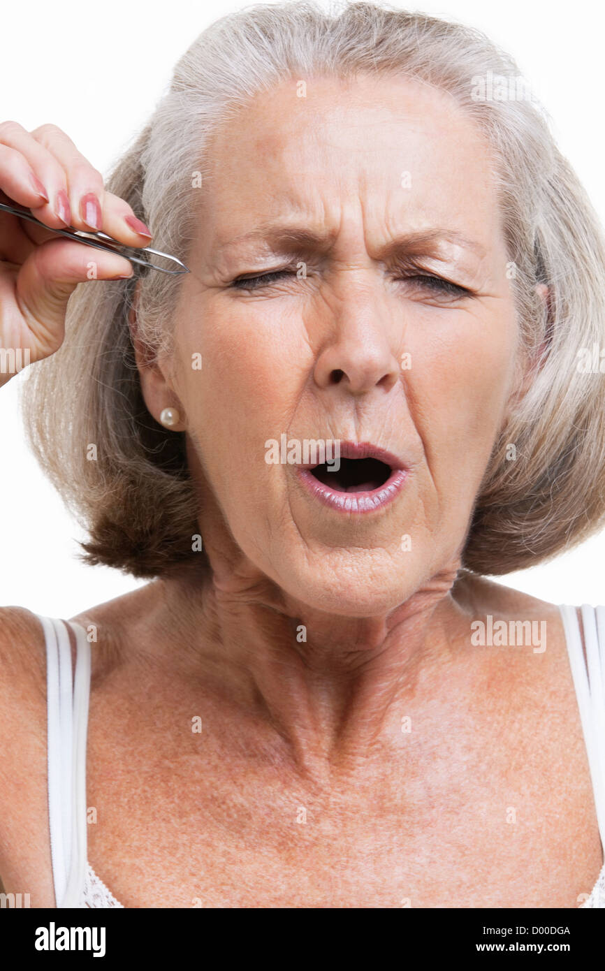 Ältere Frau tweezing Augenbrauen vor weißem Hintergrund Stockfoto