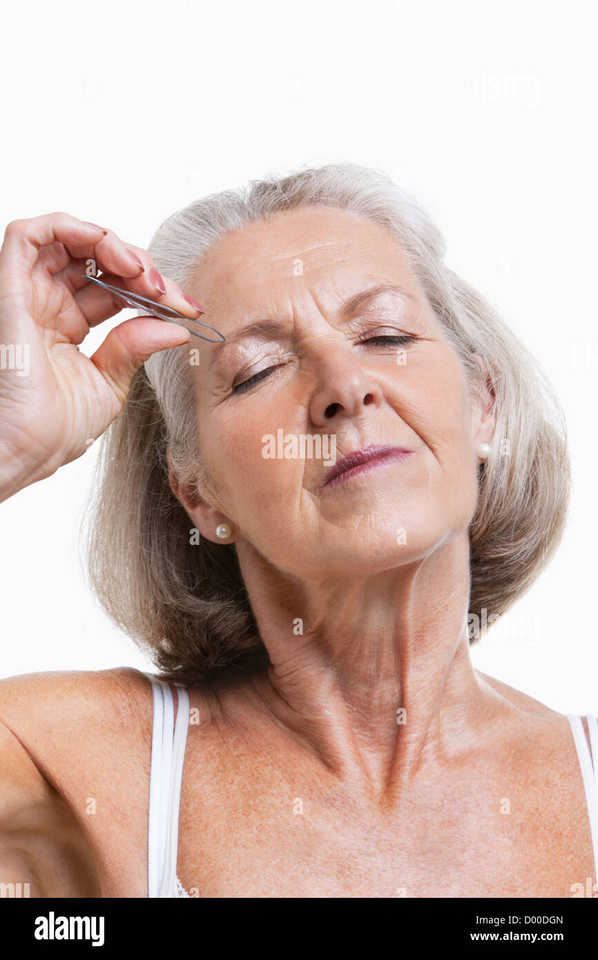 Ältere Frau tweezing Augenbrauen vor weißem Hintergrund Stockfoto