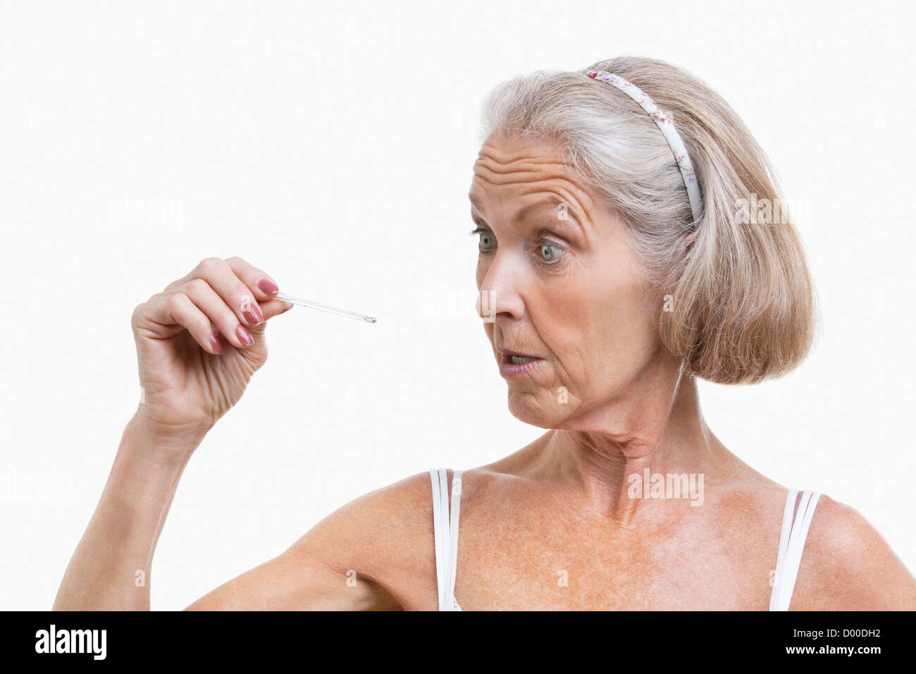 Ältere Frau prüfen Thermometer vor weißem Hintergrund Stockfoto