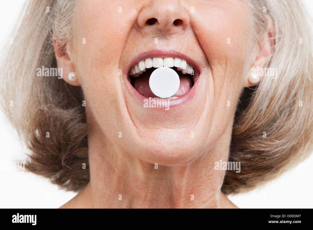 Ältere Frau mit einer Pille zwischen den Zähnen vor weißem Hintergrund Stockfoto