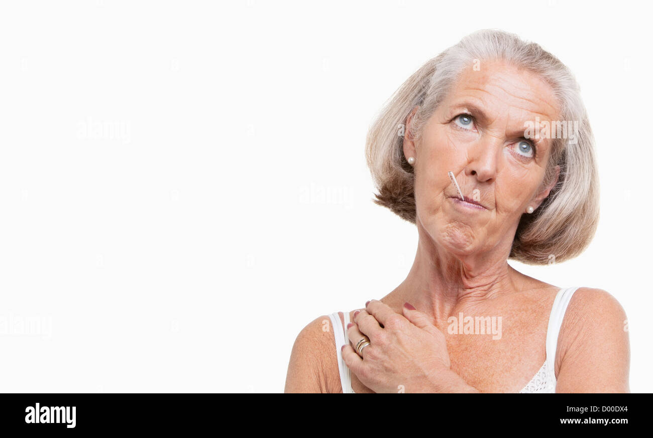 Unwohl senior Frau mit Thermometer im Mund vor weißem Hintergrund Stockfoto