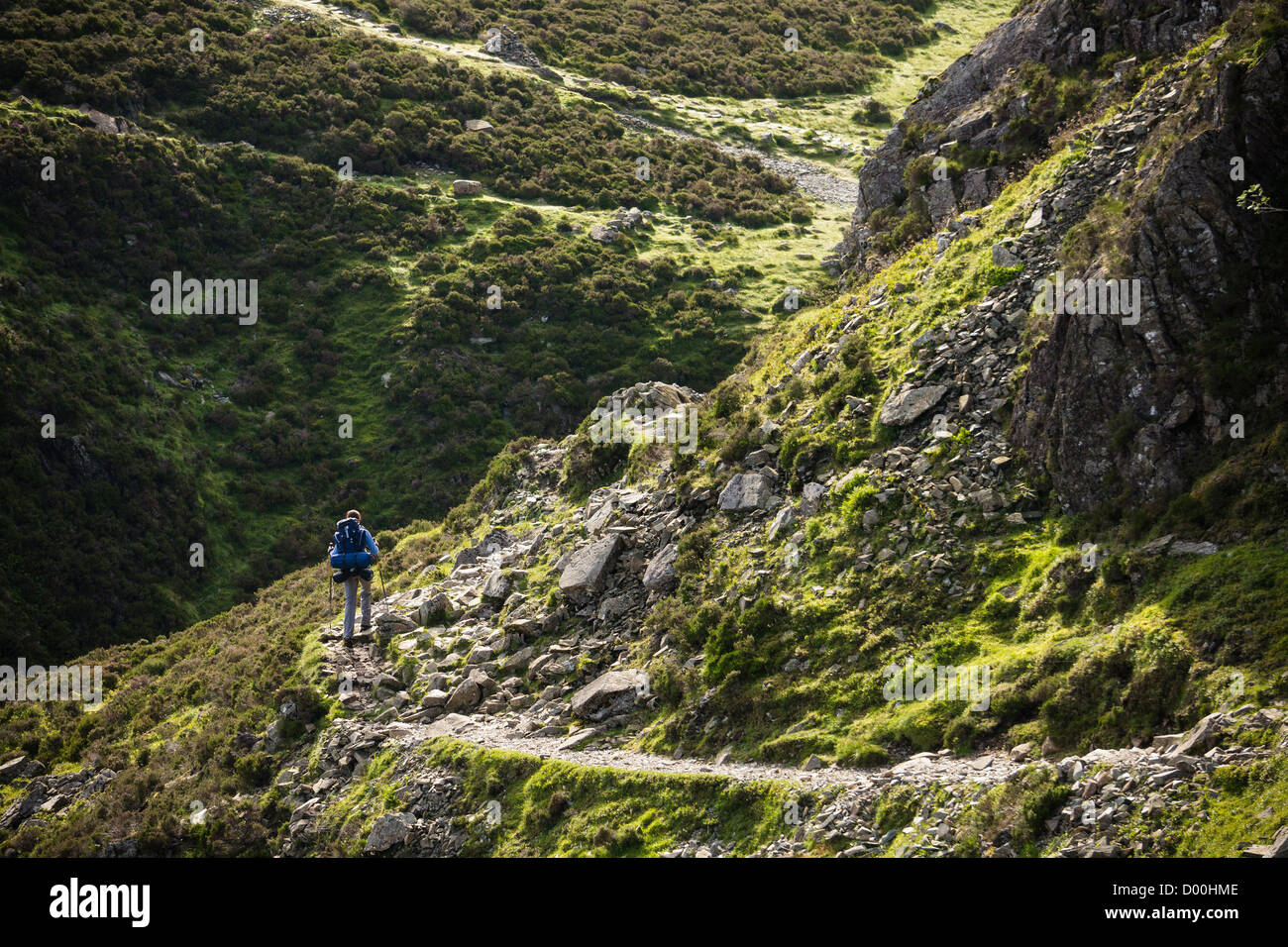 Eine Frau Wanderer zu Fuß einen Stein Weg mit einem großen Rucksack im Lake District. Stockfoto