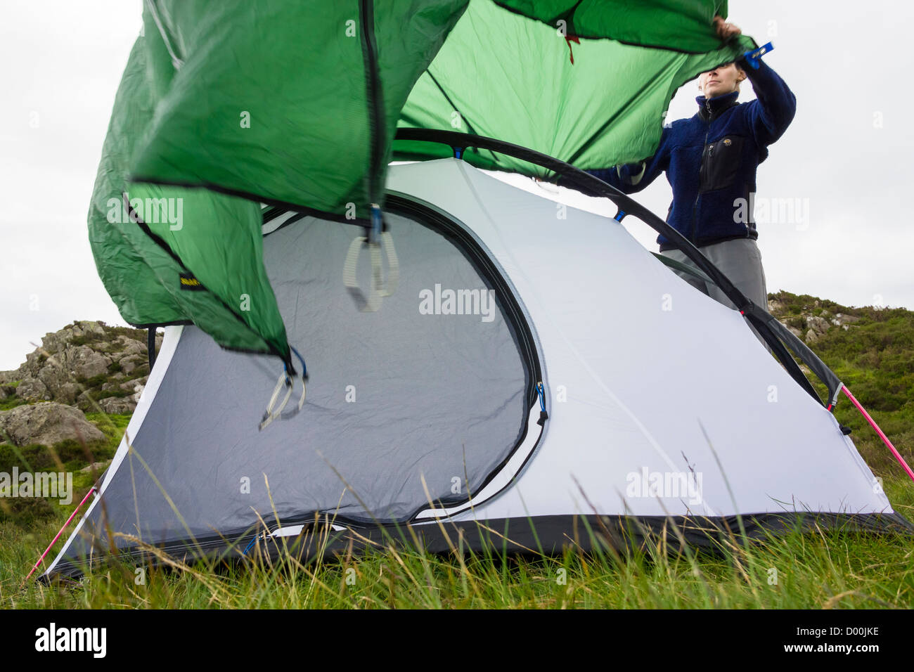 Eine Frau, eine Fliege Blatt über ein Zelt auf grasbewachsenen Boden weht. Stockfoto