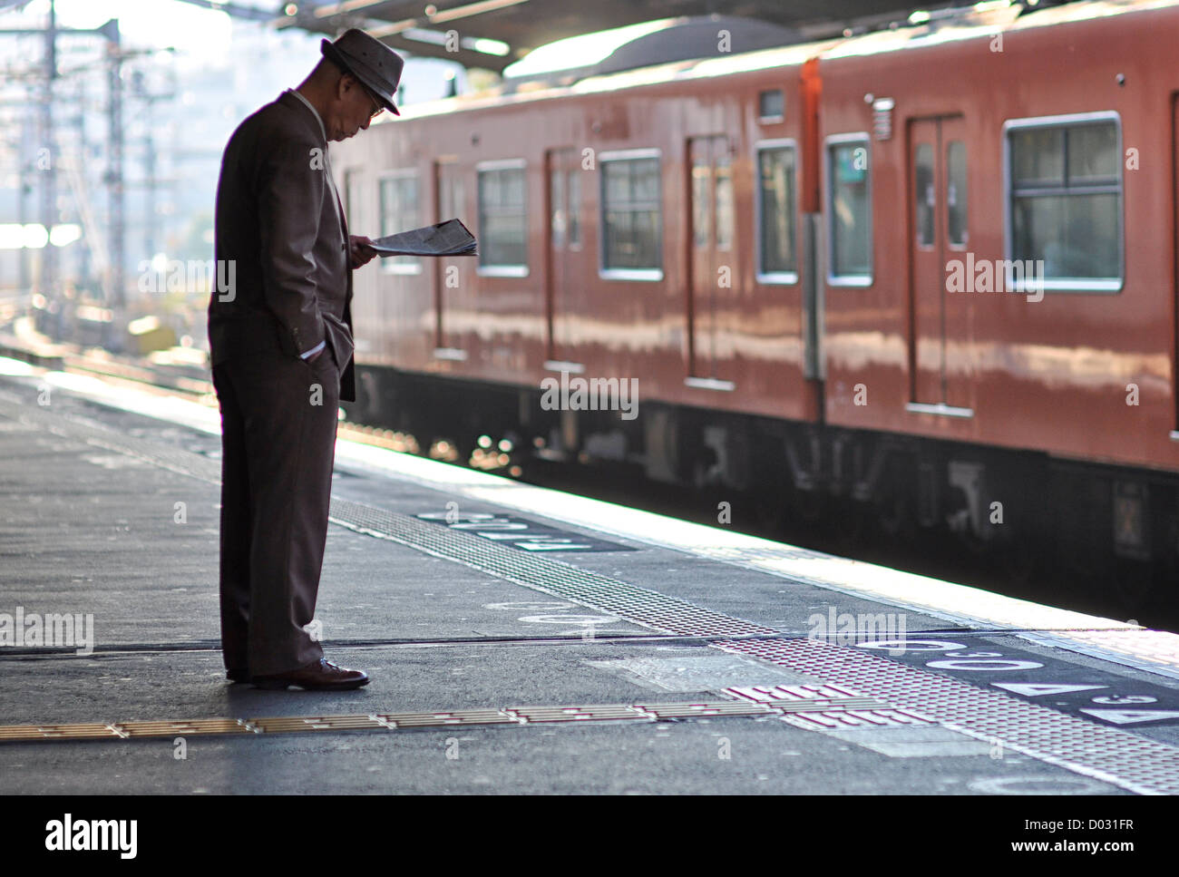 Ein älterer Mann eine Zeitung lesen, während des Wartens auf einen Zug. Stockfoto