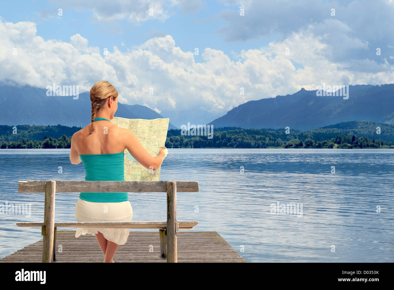 Eine junge Frau sitzt auf einer Bank vor einem See Kartenlesen Stockfoto