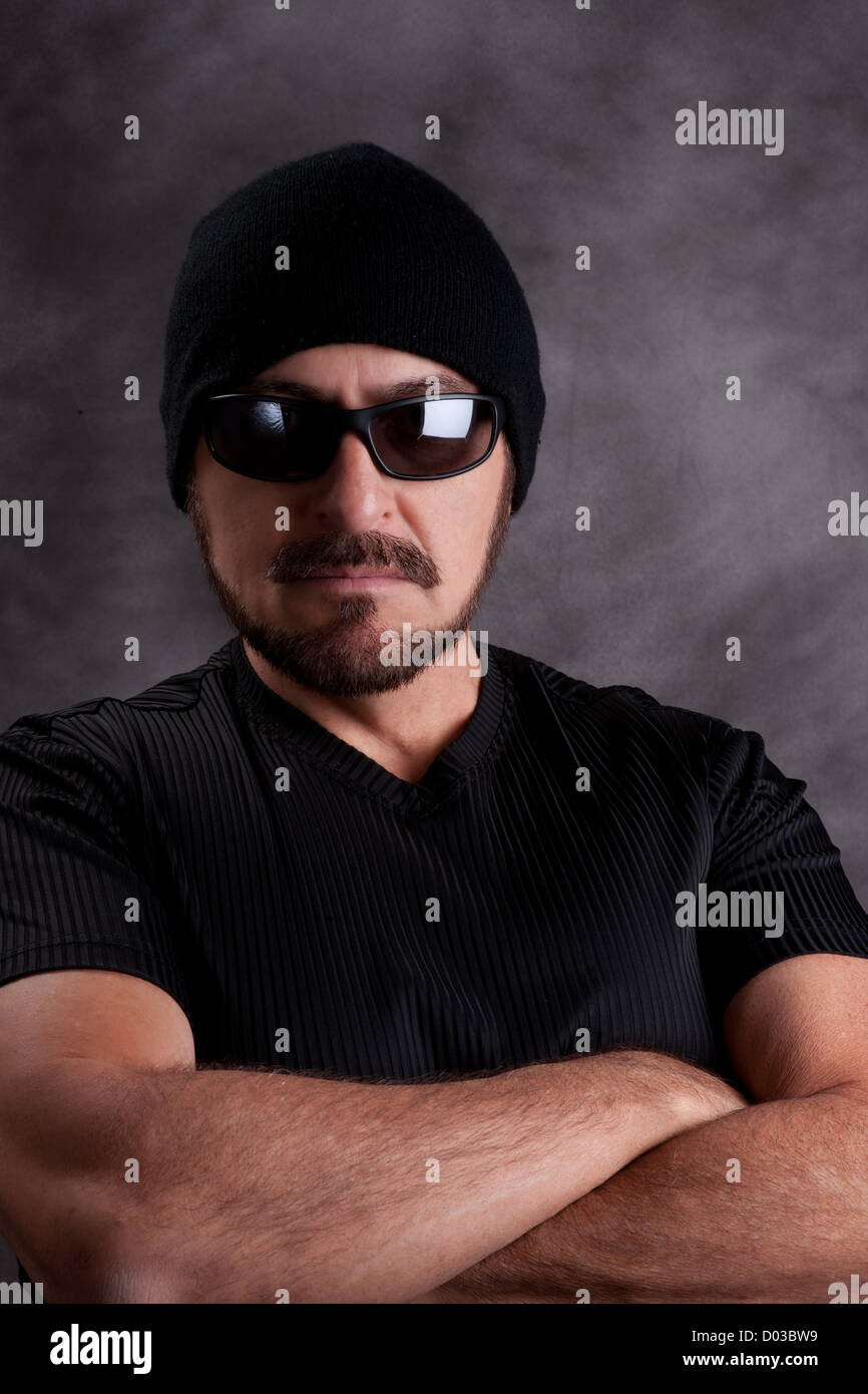 Stolz auf harter Kerl in schwarz. Starke Mann im schwarzen Hemd, Sonnenbrille und Zipfelmütze mit muskulösen Arme verschränkt, gerichtete Kamera Stockfoto