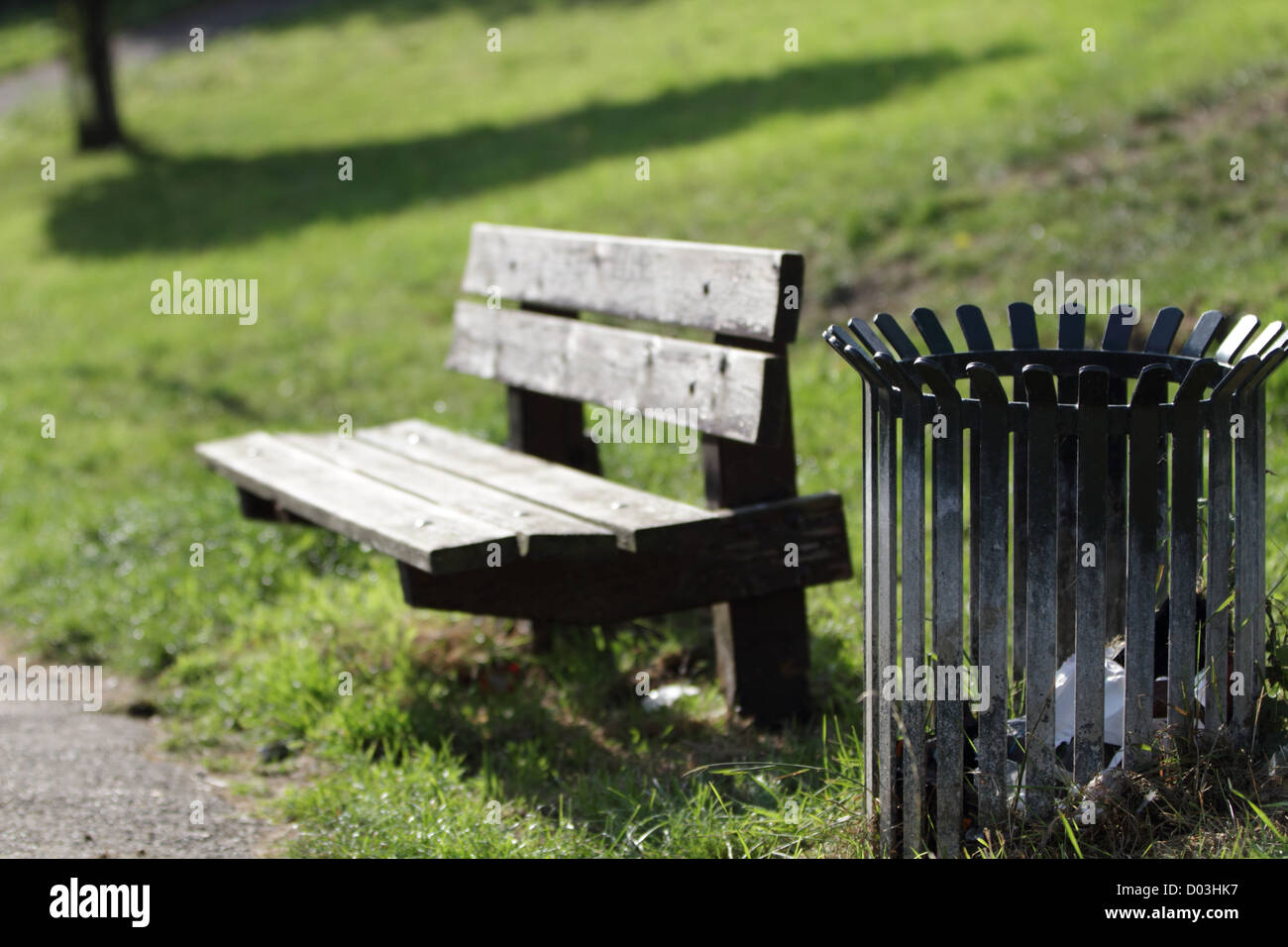 Eine krumme Woorden Parkbank neben einem Metall Abfallbehälter an einem sonnigen Nachmittag in einem Park in Maastricht. Stockfoto