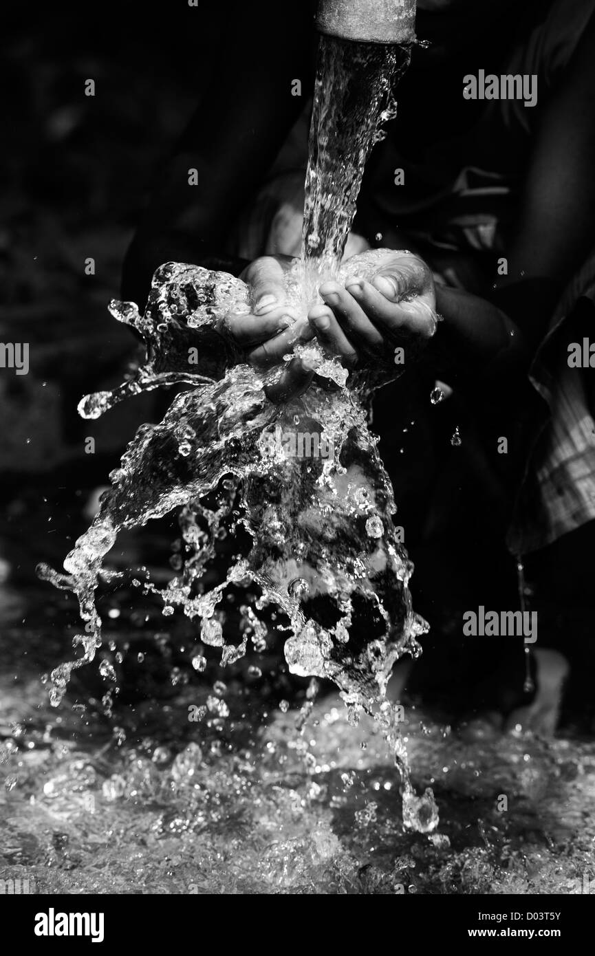 Wasser aus einer Handpumpe in einem indischen Dorf Gießen in eine indische Mädchen Hände. Andhra Pradesh, Indien. Monochrom Stockfoto
