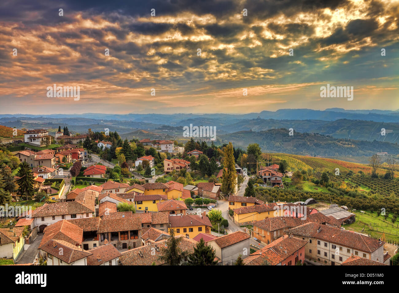 Luftbild auf italienischen Kleinstadt zwischen Hügeln unter schönen herbstlichen Wolkenhimmel bei Sonnenuntergang im Piemont, Norditalien. Stockfoto