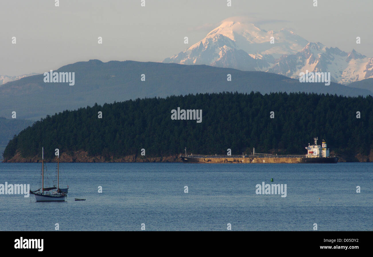 Ein Segelboot und eine große kommerzielle Schiff schweben in Peters Bay in der Nähe von Sonnenuntergang, mit den Cascade Mountains im Hintergrund. Stockfoto