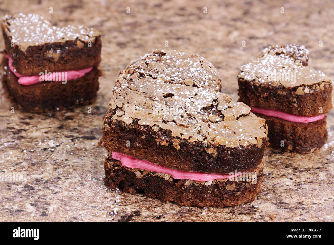 Drei köstliche Brownies in Herzform mit Erdbeeren oder Himbeeren aromatisierten Glasur geleitet. Stockfoto