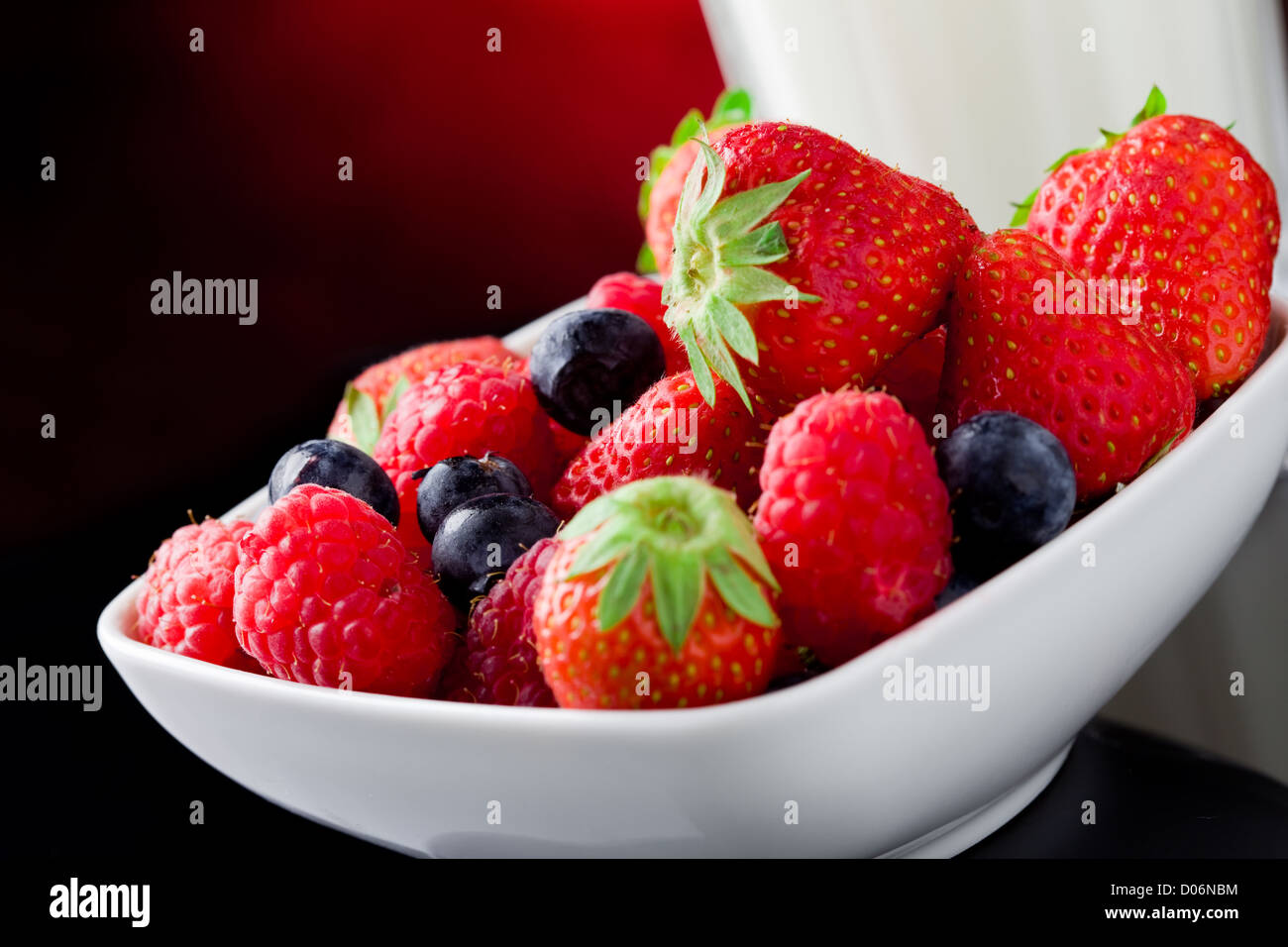 Foto von Milchglas mit Beeren auf rot beleuchteten Hintergrund Stockfoto