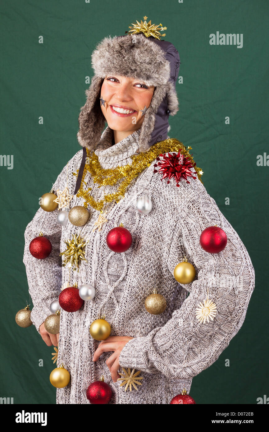 Hübsche junge Frau stolz lächelnd posiert wie ein geschmückter Weihnachtsbaum, lustige Xmas Studio Aufnahme vor einem grünen Hintergrund Stockfoto