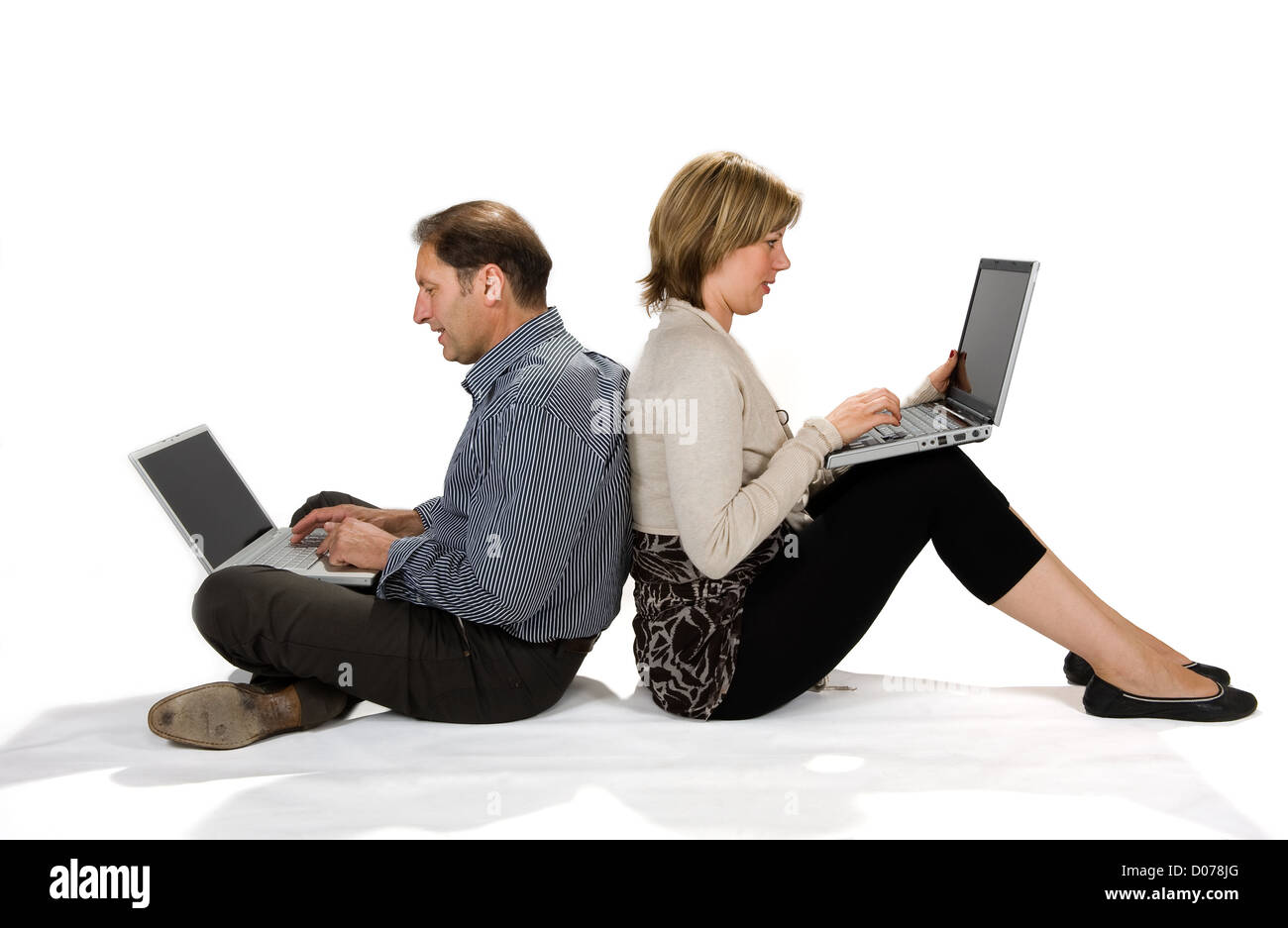 Ein paar sitzt auf dem Boden sowohl auf als auch auf dem Laptop arbeiten Stockfoto
