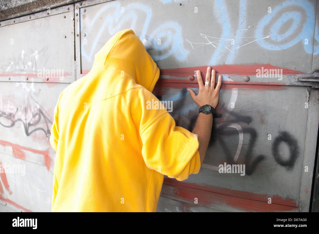 Junger Mann in Sweatshirt mit Kapuze / Jumper Grunge Graffitiwand zeigend. Konzeptionelle Stockfoto