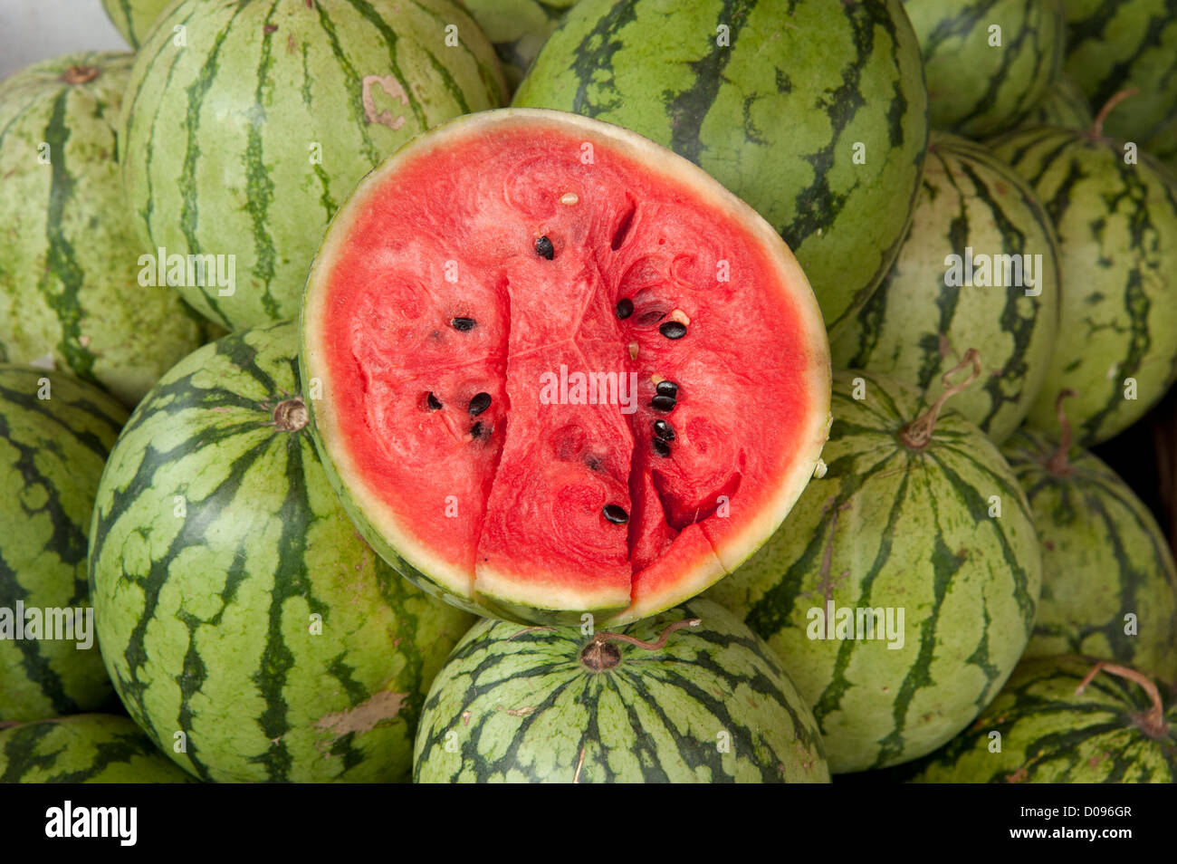 Nahaufnahme der roten Innenseiten einer in Scheiben geschnittenen Wassermelone Hälfte auf viele grüne Wassermelonen zum Verkauf in Kandy Sri Lanka Stockfoto