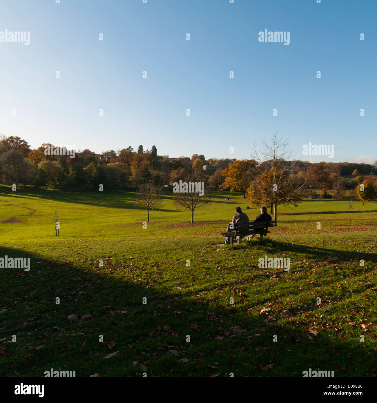 Herbstszene im Gadebridge Park, Hemel Hempstead, Hertfordshire, Großbritannien. 2 Personen auf einer Bank genießen die Landschaft. Stockfoto