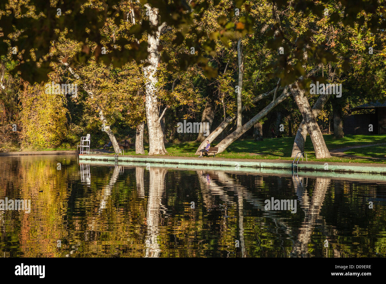 Ein Blick auf die Badestelle im Fluss in Bidwell Flusspark mit Reflexionen und ein Mann entspannend auf Parkbank in Chico CA. Stockfoto