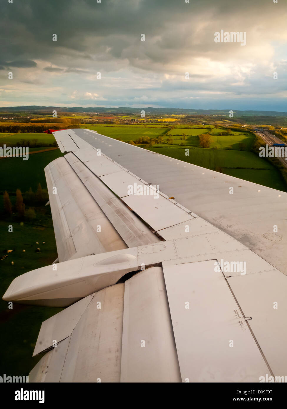 Flügel der Boeing 737 Verkehrsflugzeug Tiefflug auf endgültige Abstieg mit Landschaft, Felder und stürmischen Himmel Stockfoto