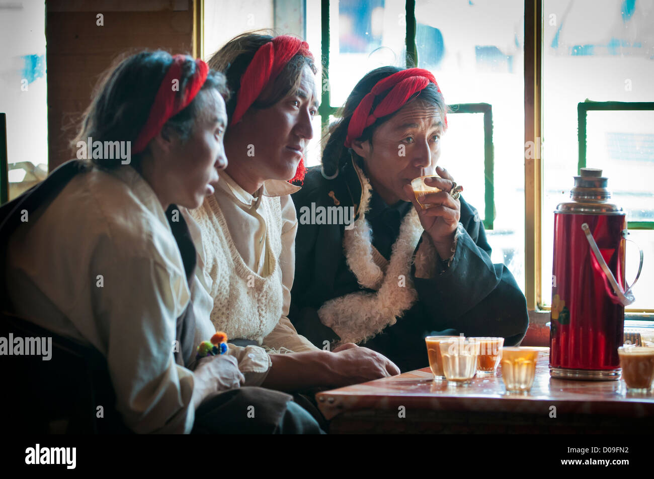 Ihre Haare geflochten und Sheap Haut Mäntel tragen, tibetische Hirten trinken Yak Buttertee im Straßencafé, Namtso, Tibet, China Stockfoto