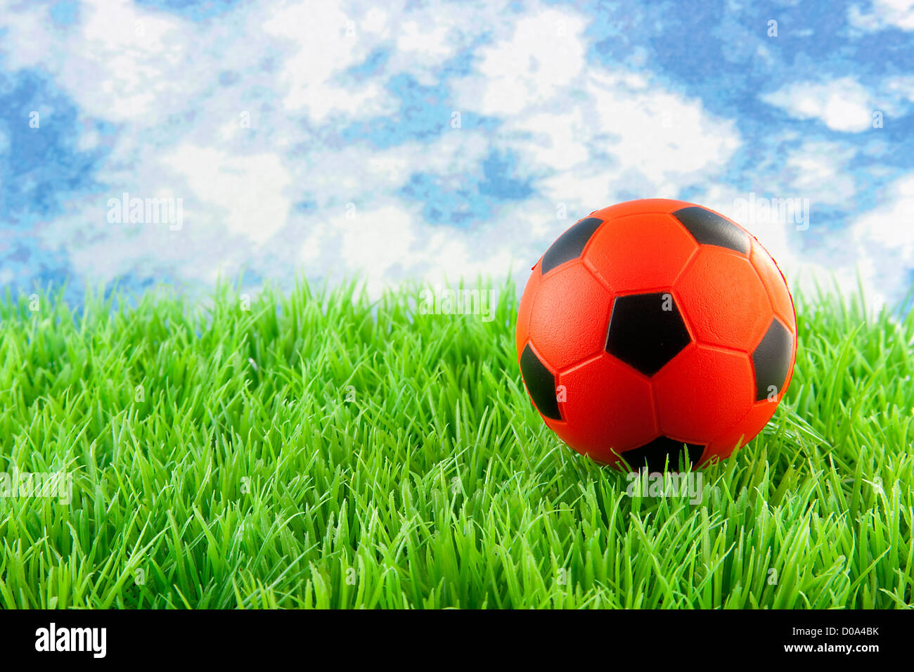 Orange Fußball auf dem Rasen gegen blauen Wolkenhimmel Stockfoto