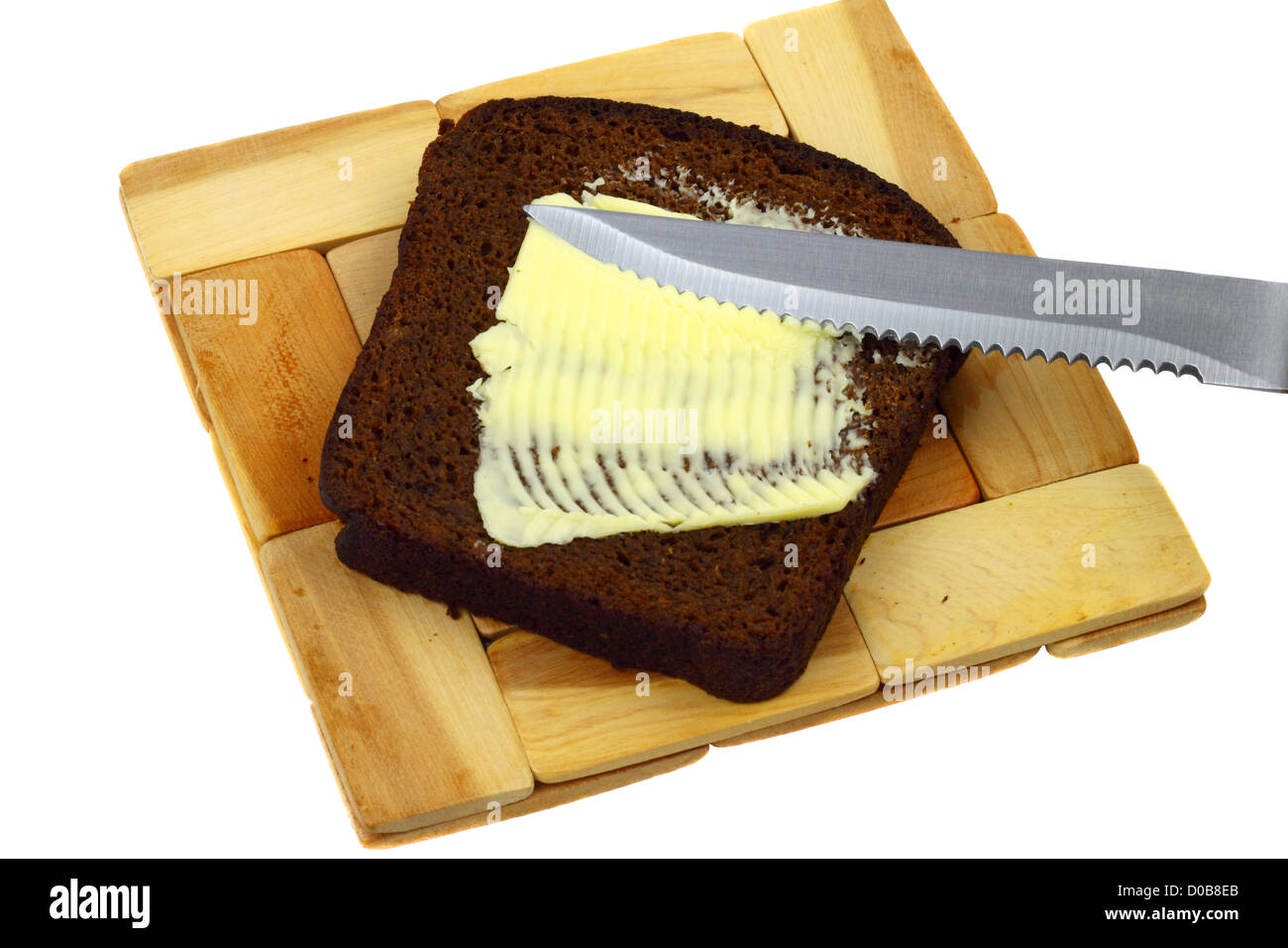 Messer schmiert Butter auf ein Stück Schwarzbrot auf ein Holzbrett, isoliert auf weiss liegend Stockfoto