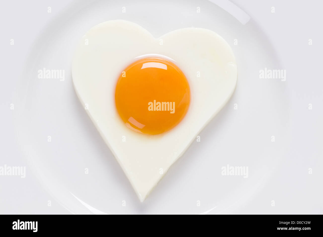 Gebratenes Ei oder Spiegelei in der Form eines Herzens auf eine weiße geformte Kreisplatte. Ei präsentiert weiche "sunny Side up" "Eggs up" Stockfoto