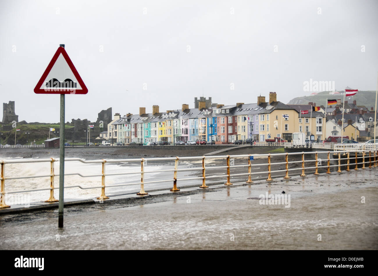 ABERYSTWYTH, Wales - einem windigen und nassen Sturm peitschen die bunten Häuser am Wasser in Aberystwyth an der Westküste von Wales. Meer Wasser Runden über dem Meer an der Wand, das Überschwemmen der Parkplatz im Vordergrund. Stockfoto