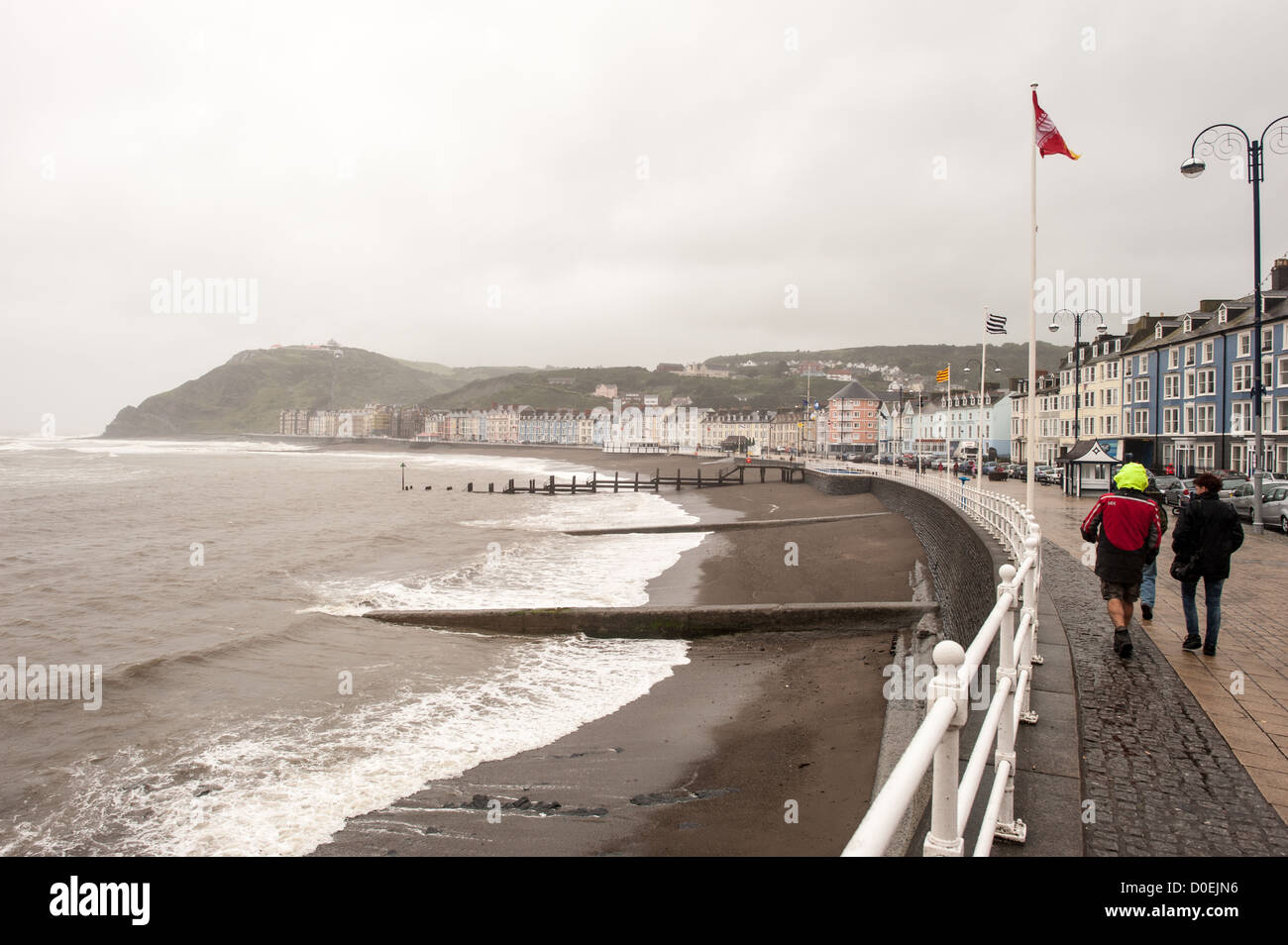 ABERYSTWYTH, Wales - ein paar Fußgänger trotzen dem windigen und nassen Wetter an der Küste von Galway an der Westküste von Wales zu gehen. Stockfoto