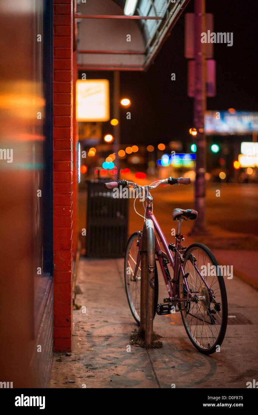Rosa Fahrrad eingesperrt auf einem Bürgersteig von Shop Schilder beleuchtet Stockfoto