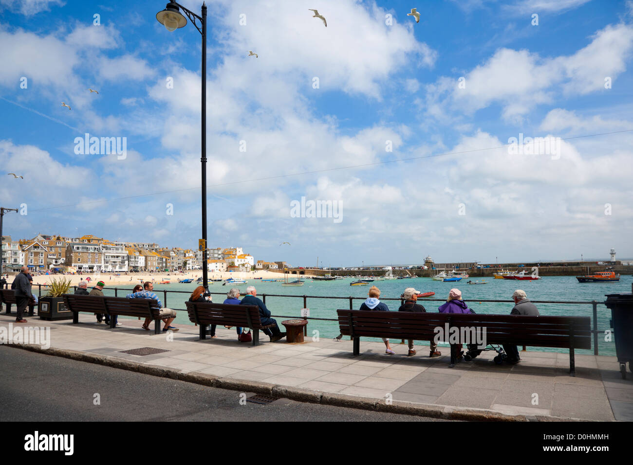 Menschen sitzen auf der Promenade am St Ives an einem sonnigen Tag. Stockfoto